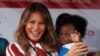 លោកជំទាវ Melania Trump ពរទារកមួយ អំឡុងពេលដំណើរទស្សនកិច្ចទៅកាន់​មន្ទីរពេទ្យ​មួយ នៅ​ប្រទេស​ហ្គាណា កាលពីថ្ងៃទី០២ ខែតុលា ឆ្នាំ២០១៨។ 