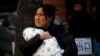 FILE - A mother carries her baby wrapped in a blanket in Beijing.
