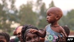 FILE - A woman holds a child on her shoulders in an internally displaced persons camp outside the town of Bunia, in Ituri province, June 21, 2019.
