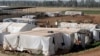 Syrian refugees walk outside their tents at a Syrian refugee camp in the eastern Lebanese town of Majdal Anjar, Lebanon, June 19, 2014.